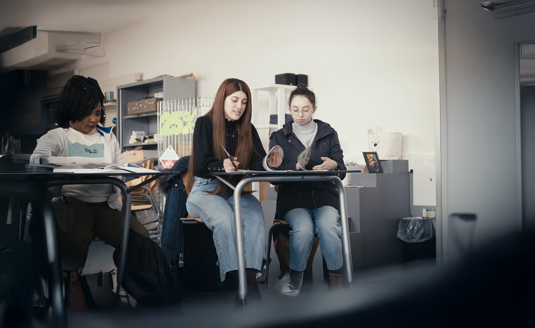 Drie studentes zitten in een klaslokaal aan hun tafel te werken.